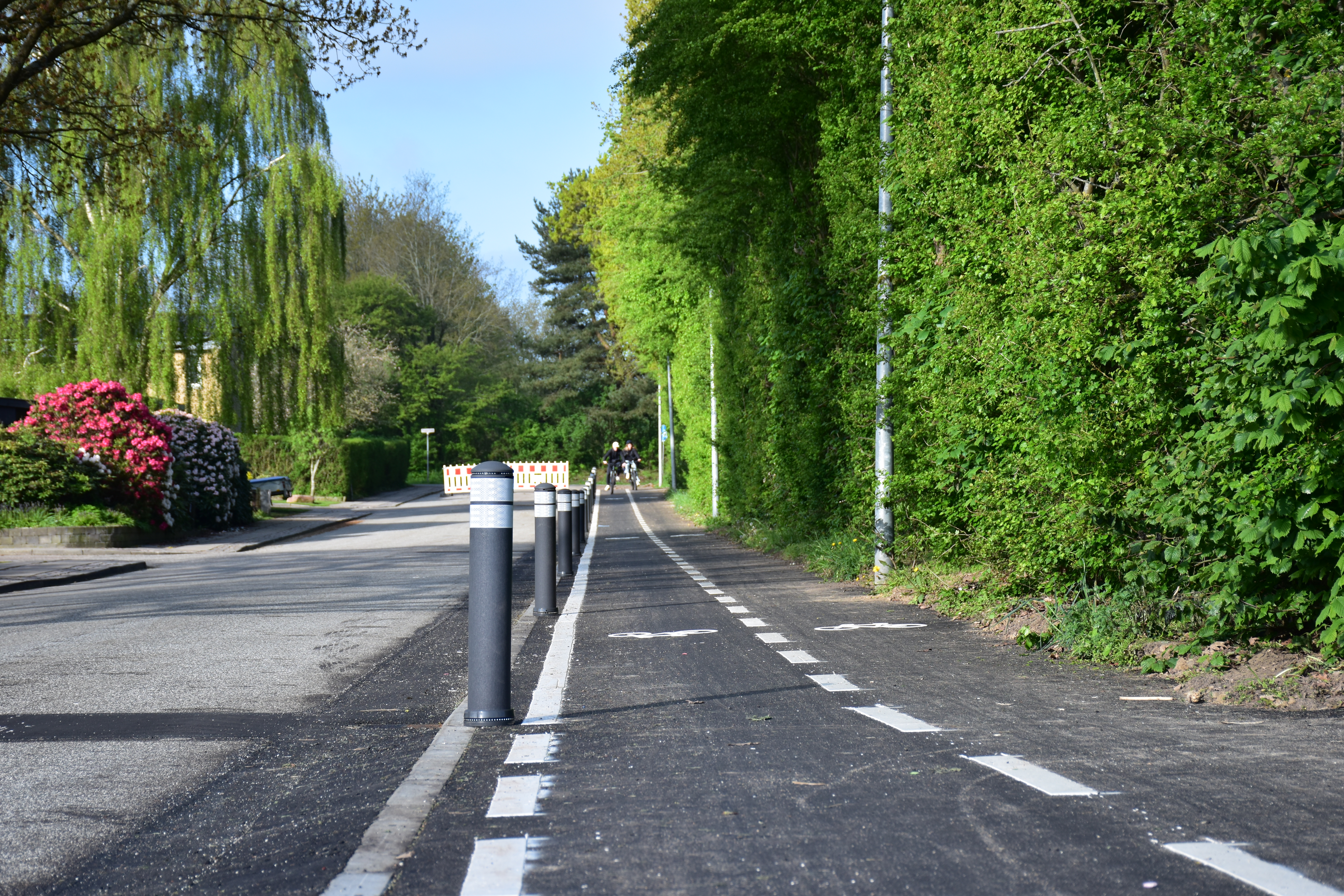 Foto af vej med nyanlagt dobbeltrettet asfaltcykelsti og et par cyklister i det fjerne.